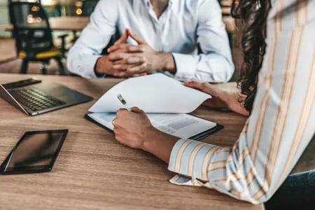 2 people at a desk having a business meeting, the one in a striped shirt signs paperwork