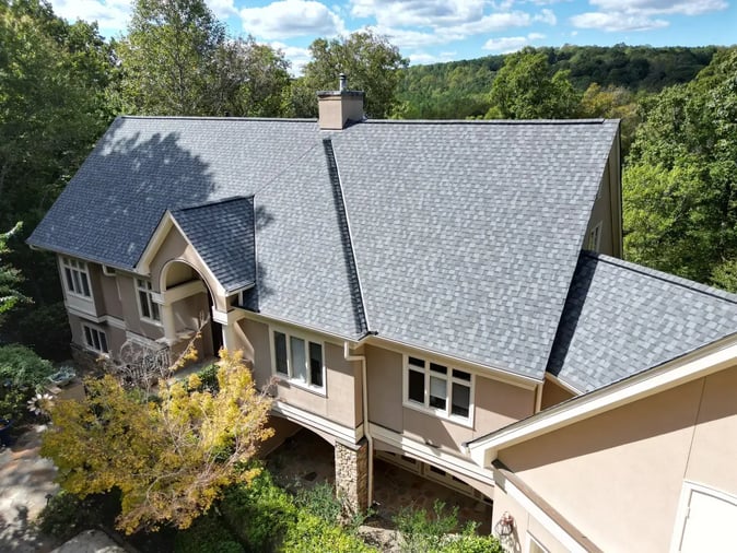 Completed gray shingle re-roof on a luxury estate in Chapel Hill's Governors Club — front elevation with arched entry and wooded hillside backdrop