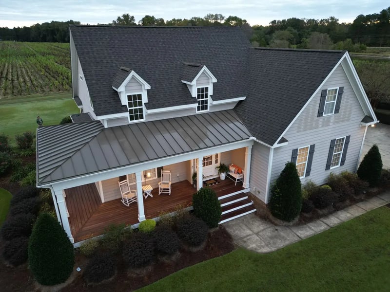 Aerial view of completed dark gray shingle roof with metal porch roof on a farmhouse-style home in Holly Springs, NC