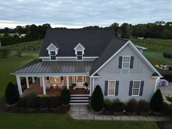Completed shingle and standing-seam re-roof on a farmhouse-style home in Holly Springs, NC — twilight front elevation with covered porch