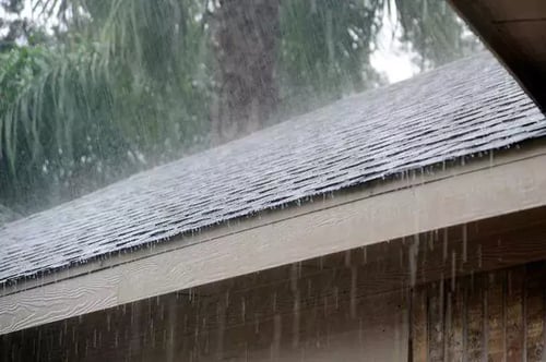 heavy rain pouring and running off the side of a shingled roof