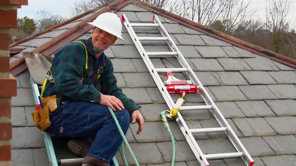 A man on a roof, fully equipped with modern safety gear and equipment