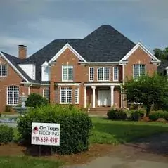 A nice brick house with a beautiful asphalt shingle roof. There is an On Tops Roofing Yard sign at the end of the driveway._WebP