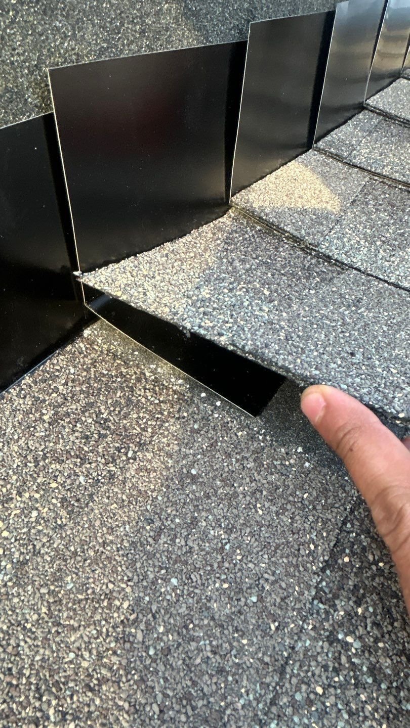 Step flashing installed correctly at a wall during a roof replacement, showing proper placement on each shingle course, new aluminum extending up the wall, and ice and water shield membrane behind the flashing
