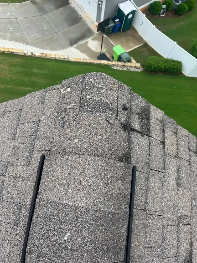 Cracked ridge cap shingles showing deterioration along the roof peak