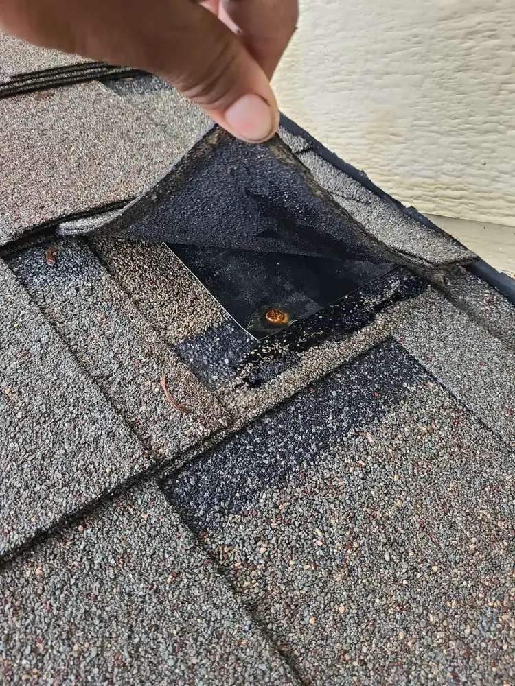 Deteriorated step flashing with rusty nail and worn sealant along roof-to-wall transition