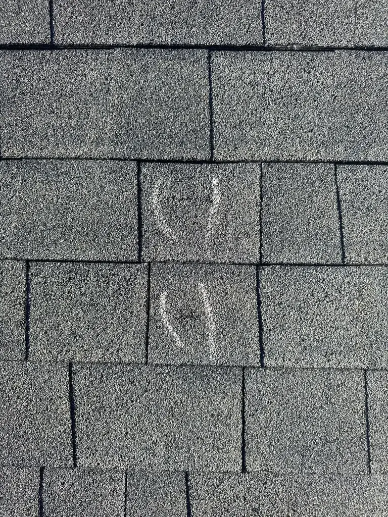 Storm-damaged shingles showing impact marks and cracking from hail