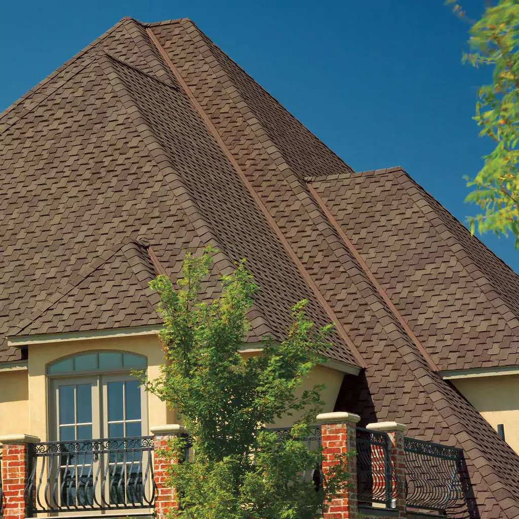 brown luxury asphalt shingles on a beige house surrounded by greenery