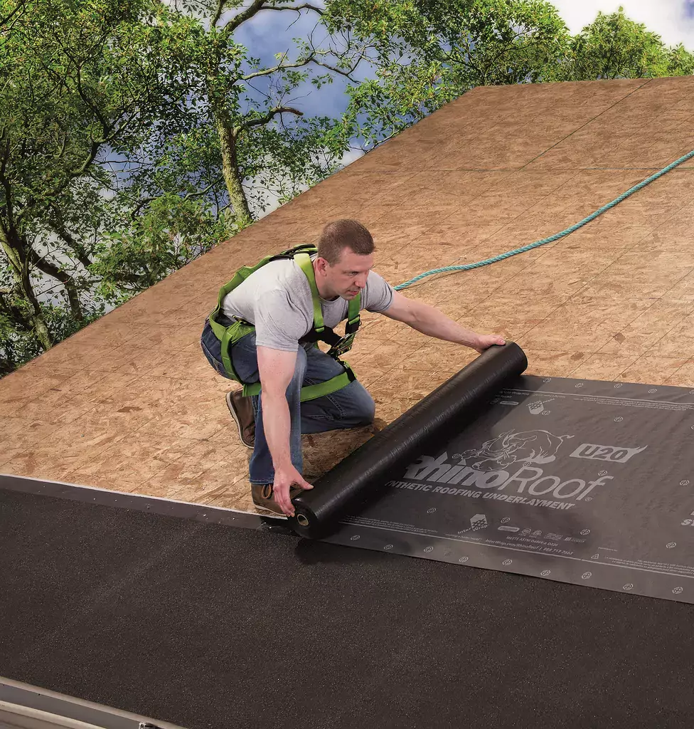 contractor laying down black underlayment on top of wooden roof decking