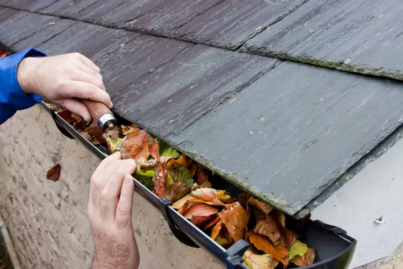 man using small shovel to remove leaves from his gutters