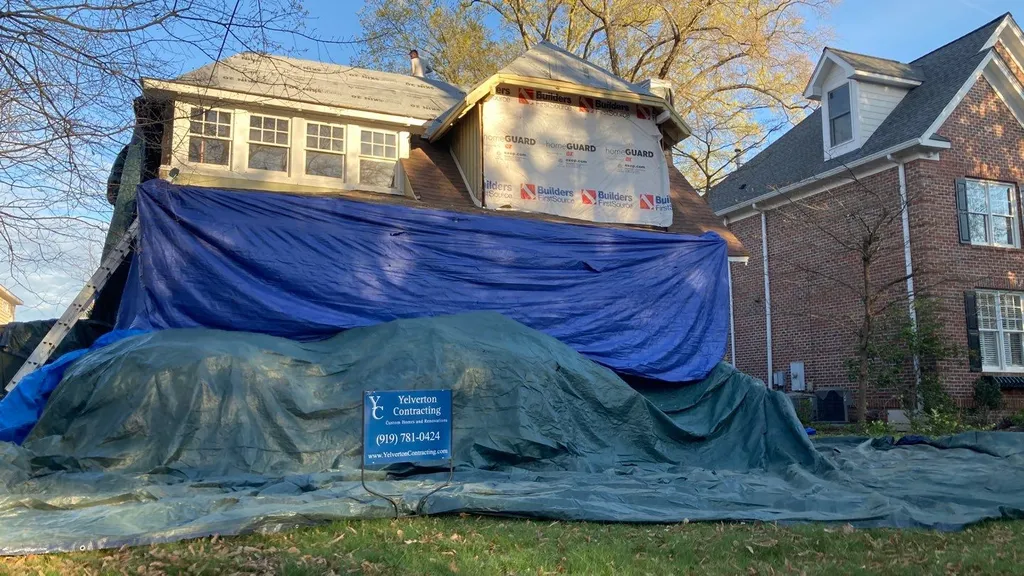 Tarps and plywood protecting landscaping and patio items during a roof replacement