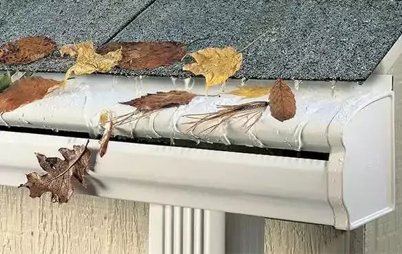 white gutter cover with brown leaves and water droplets falling down the side